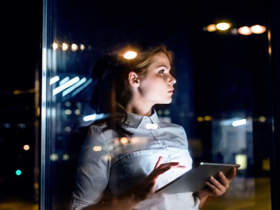 jeune entrepreneure tablette en main vue par la fenêtre de son bureau le soir